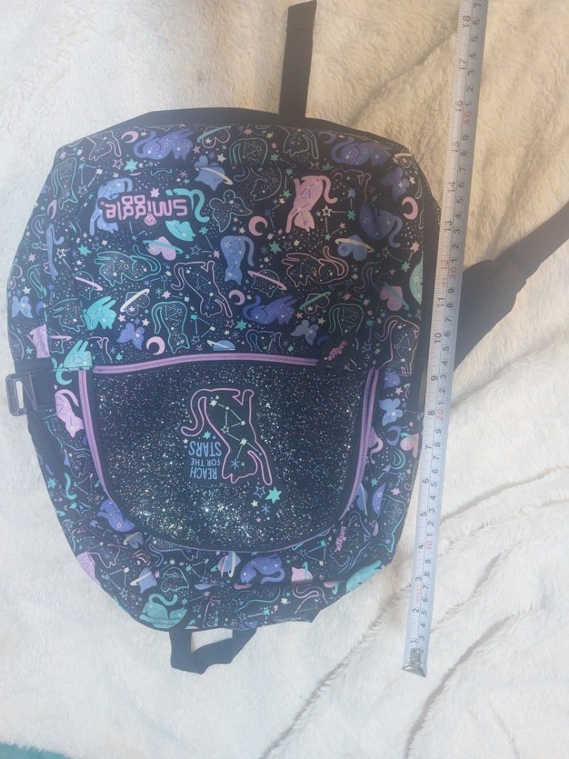 Smiggle Backpack, Pencil Case, id holder, and Wallet Set (Category: Babies & Kids Fashion) located in Taguig. Submitted by felixfelicis11 (Listing ID 1441886388, Image 3). Description: - Adorable Smiggle backpack with 'Reach for the Stars' cat design. - Black backpack with glitter and fun cat/moon prints. - Includes a Smiggle fruit-themed pencil case. - Matching pink wallet with a sparkly ice cream design. - Ideal for school, travel, or everyday 