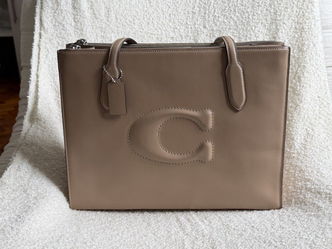 Coach Tote Bag with Embossed C Logo (Category: Luxury Bags & Wallets) located in Pateros City. Submitted by angelicabo (Listing ID 1442047965, Image 1). Description: - Taupe Coach tote bag - Large embossed C logo on front - Zip-top closure - Two top handles - Includes small leather hangtag - Ideal for everyday use.