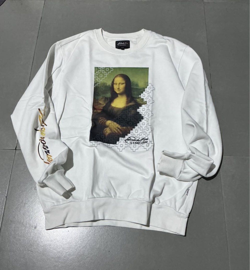 White Mona Lisa Graphic Sweatshirt (Category: Coats, Jackets and Outerwear) located in Manila. Submitted by irthrift (Listing ID 1441970792, Image 2). Description: - White long-sleeve sweatshirt - Features iconic Mona Lisa graphic print on front - Unique geometric pattern detail on side and sleeve - Perfect addition to any collection.
