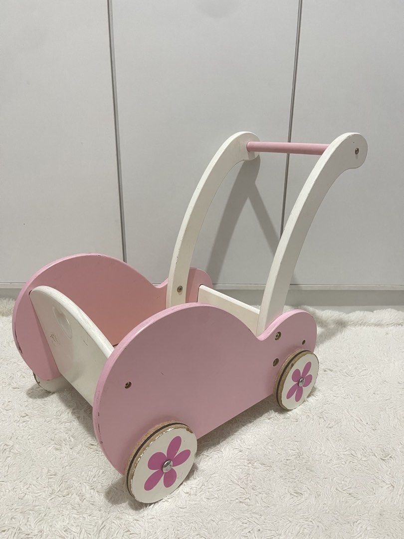 Wooden Viga doll stroller/cart (Category: Strollers) located in Manila. Submitted by jassie06 (Listing ID 1442074237, Image 1). Description: NEEDS CLEANING. SUPER NICE 🩷 This wooden Viga doll stroller is designed in pink and white with a charming flower motif on the wheels. Brand and Model: Viga 50176 Baby Doll Stroller Buggy. Key Details: Features include a heart-shaped cutout on the back, shock-absorbing rubber rings on the wheels to protect f