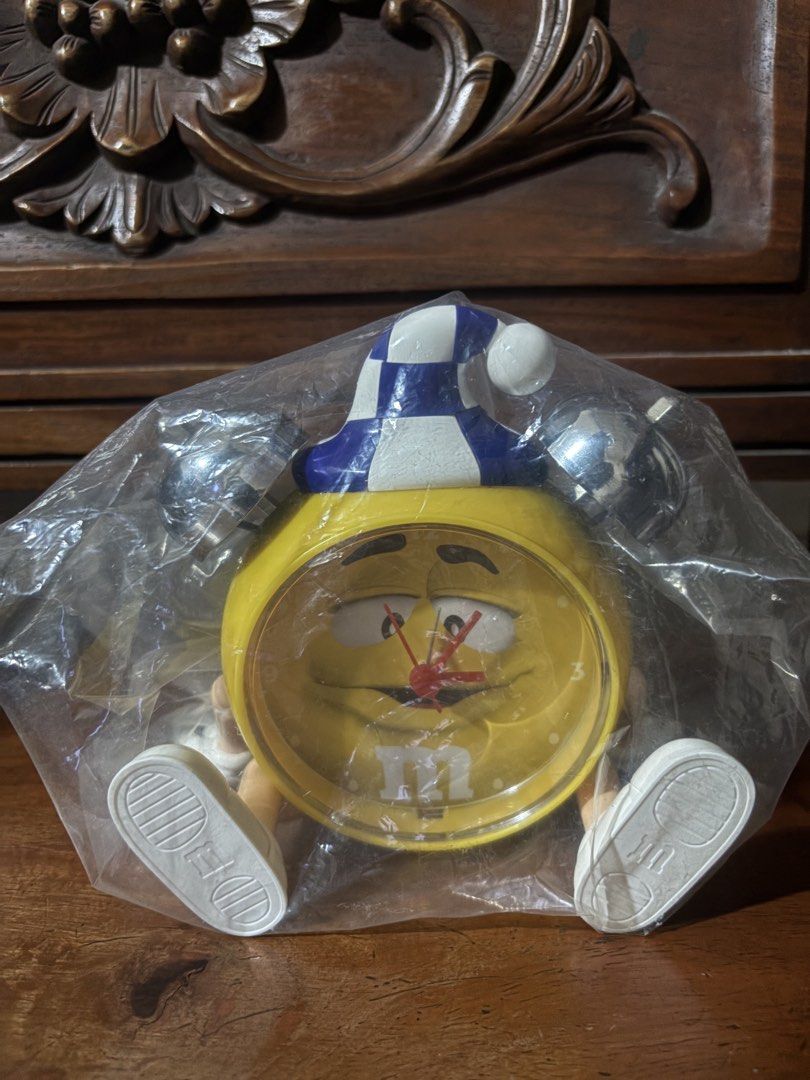 M&M Yellow Character Alarm Clock with Bell (Category: Clocks) located in Cavite. Submitted by axeliz (Listing ID 1442331068, Image 2). Description: - Adorable M&M alarm clock featuring the yellow character in a sleeping cap. - Equipped with two loud bells on top and cute little legs. - Battery operated for convenient placement. - Tested and confirmed to be in good working condition. - Ideal gift for M&M enthusiasts or a fun addition to any desk s