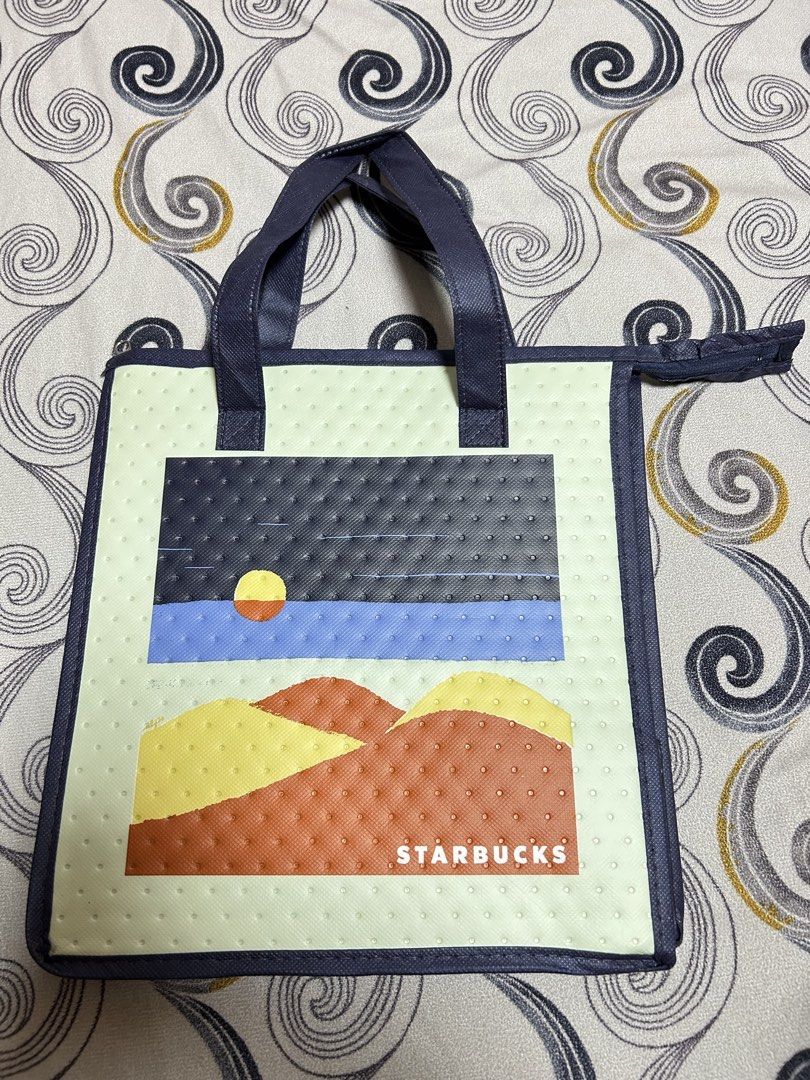Starbucks Cooler Bag with Landscape Design (Category: Water Bottles & Tumblers) located in Manila. Submitted by wabiske (Listing ID 1442306380, Image 1). Description: - Cute Starbucks cooler bag - Features a scenic landscape print (mountains, sunset over water) - Navy blue handles and trim - Zipper closure - Ideal for picnics or keeping drinks cool -Unused.