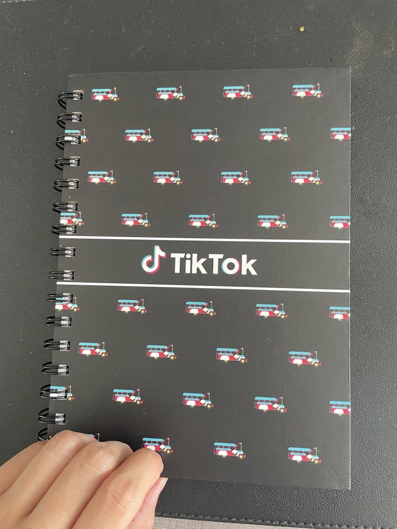 TikTok Spiral Notebook with Bus Design (Category: Stationery & School Supplies) located in Quezon City. Submitted by andreaaa_______ (Listing ID 1442246487, Image 2). Description: - Black spiral notebook ring - Features a repeating pattern of red and blue buses - Prominent TikTok logo in the center - Lined pages - Still in original plastic packaging B5 size.