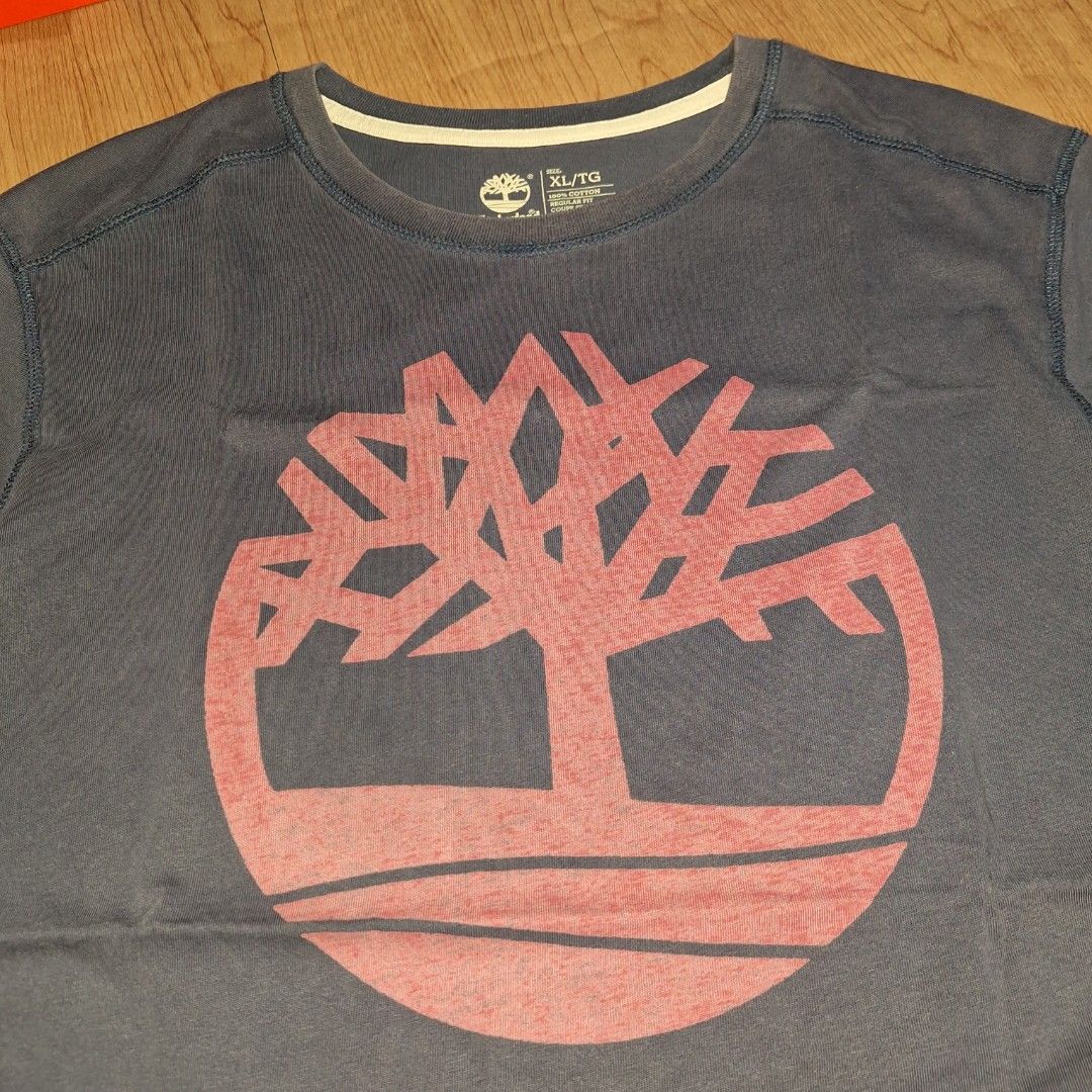 Timberland Big Logo (Category: Tshirts & Polo Shirts ) located in Aroroy. Submitted by rewear_r3volution (Listing ID 1442330139, Image 2). Description: This is a navy blue Timberland t-shirt featuring a prominent red tree logo on the chest. Size XL.