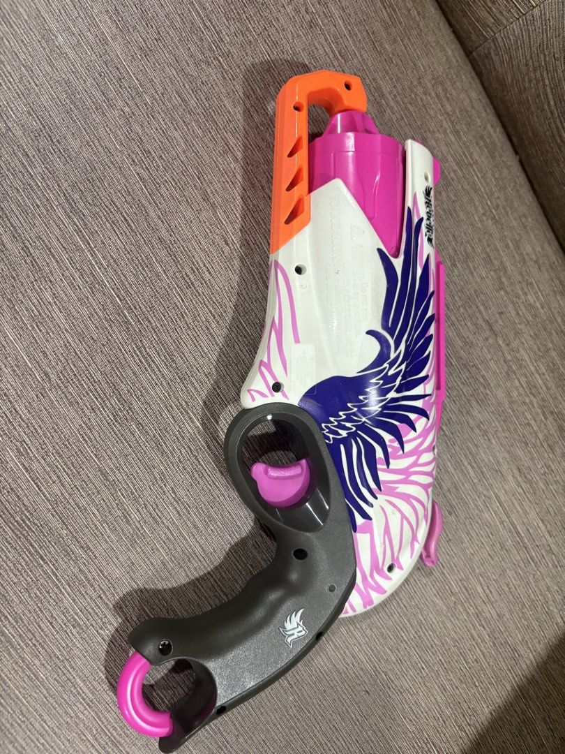 Nerf Rebelle Sweet Revenge blaster (Category: Cases & Sleeves) located in Manila. Submitted by dig76 (Listing ID 1442442677, Image 2). Description: This is a Hasbro Nerf Rebelle Sweet Revenge blaster, featuring a white and pink design with purple wing graphics and a 5-dart revolving barrel. The blaster is designed for hammer-action firing and can reach distances of up to 75 feet..