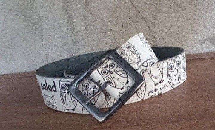 SALAD OWL WHITE PRINTED LEATHER BELT (Category: Activewear) located in Lamut. Submitted by sakosack (Listing ID 1442376871, Image 2). Description: Unique belt featuring an owl print design. The belt has a square buckle and a blue tag. The brand name "Salad" is visible on the belt. The belt's interior is a dark grey color. The belt has a "birds paradise" tag..