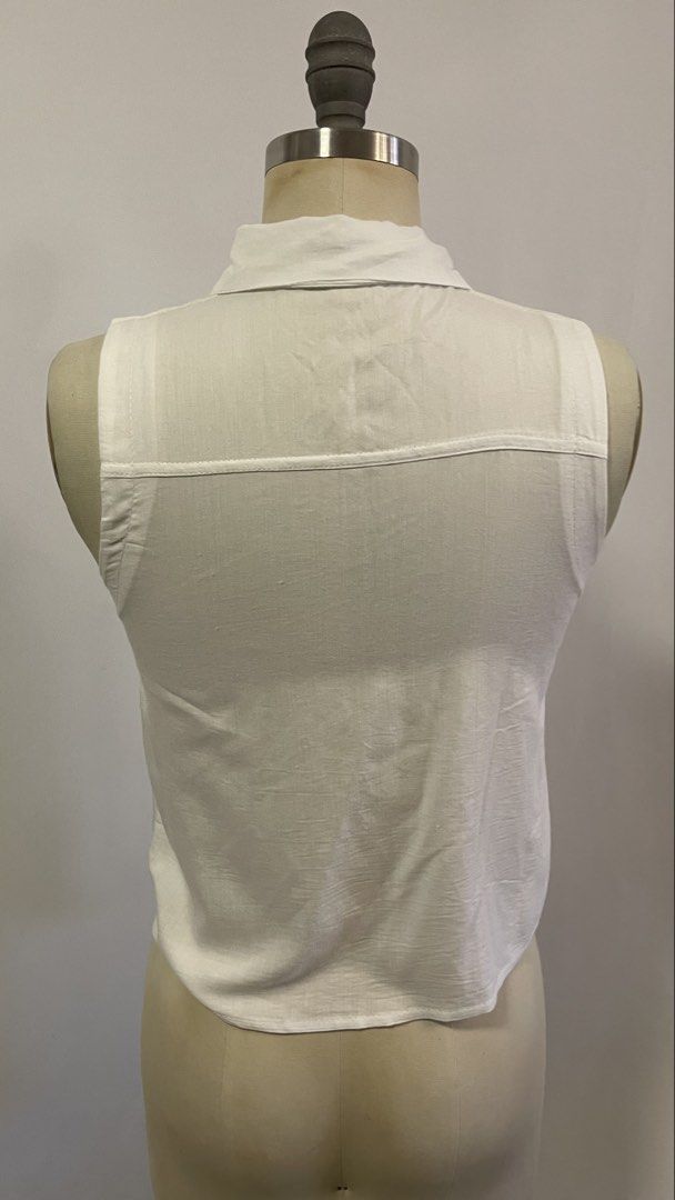 White Sleeveless Button-Up Shirt with Tie Front (Category: Blouses) located in General Trias. Submitted by 1992thelabel (Listing ID 1442466628, Image 3). Description: - Classic white sleeveless shirt - Button-up front with a left chest pocket - Unique knot detail at the bottom - Collared shirt style - Versatile and easy to pair with any outfit - Ideal for warm weather.