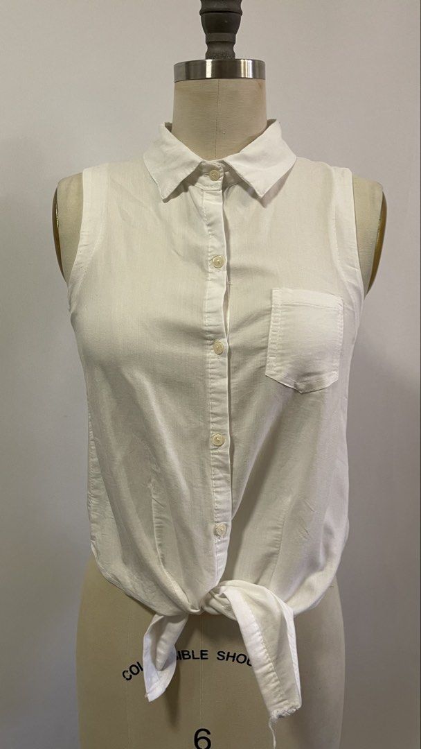 White Sleeveless Button-Up Shirt with Tie Front (Category: Blouses) located in General Trias. Submitted by 1992thelabel (Listing ID 1442466628, Image 1). Description: - Classic white sleeveless shirt - Button-up front with a left chest pocket - Unique knot detail at the bottom - Collared shirt style - Versatile and easy to pair with any outfit - Ideal for warm weather.