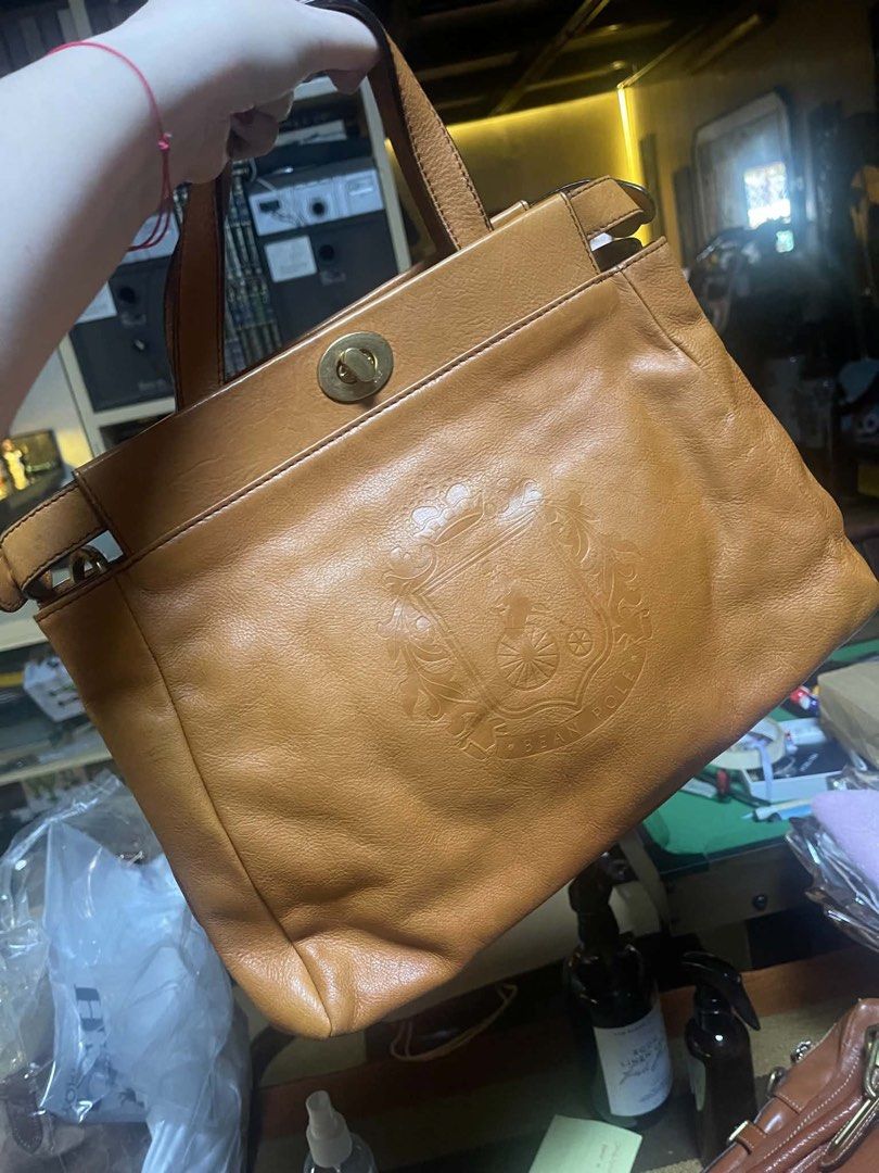 Brown Leather Handbag with Crest Emblem (Category: Luxury Bags & Wallets) located in Quezon City. Submitted by zxzye34 (Listing ID 1442720403, Image 1). Description: - Classic brown leather handbag - Prominent embossed crest emblem on the front - Secure turn-lock closure - Sturdy top handles - Rich, beautiful leather color - Ideal for everyday use or as a chic accessory.