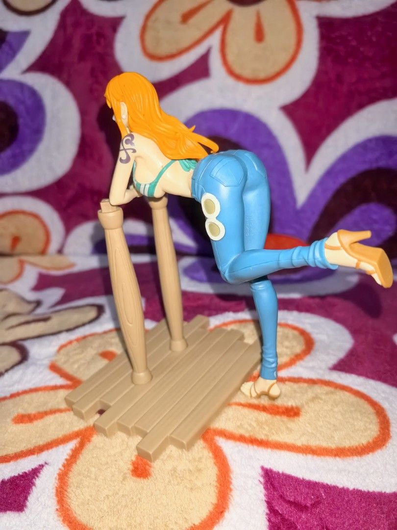 One Piece Nami Figure with Stand (Category: Figurines & Statues) located in Quezon City. Submitted by silentbozz (Listing ID 1442672576, Image 2). Description: - Authentic Nami figure from the popular anime One Piece. - Detailed design showcasing her signature orange hair and blue outfit. - Posed dynamically on a wooden stand with two supporting pillars (pero missing yung patungan sa pillars) - Base includes subtle markings pati sa figure - Selli