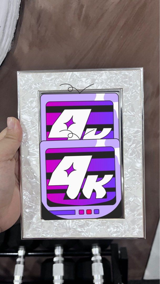 SM Home Photo Frame with 4K Design (Category: Frames & Pictures) located in Manila. Submitted by sevora (Listing ID 1442659419, Image 1). Description: - SM Home Photo Frame - Unique design with two '4K' logos - Purple and black background - Silver frame with textured white border - Built-in stand and hook for hanging - Original price tag of P499 still attached - Perfect for displaying photos or as a decorative piece.