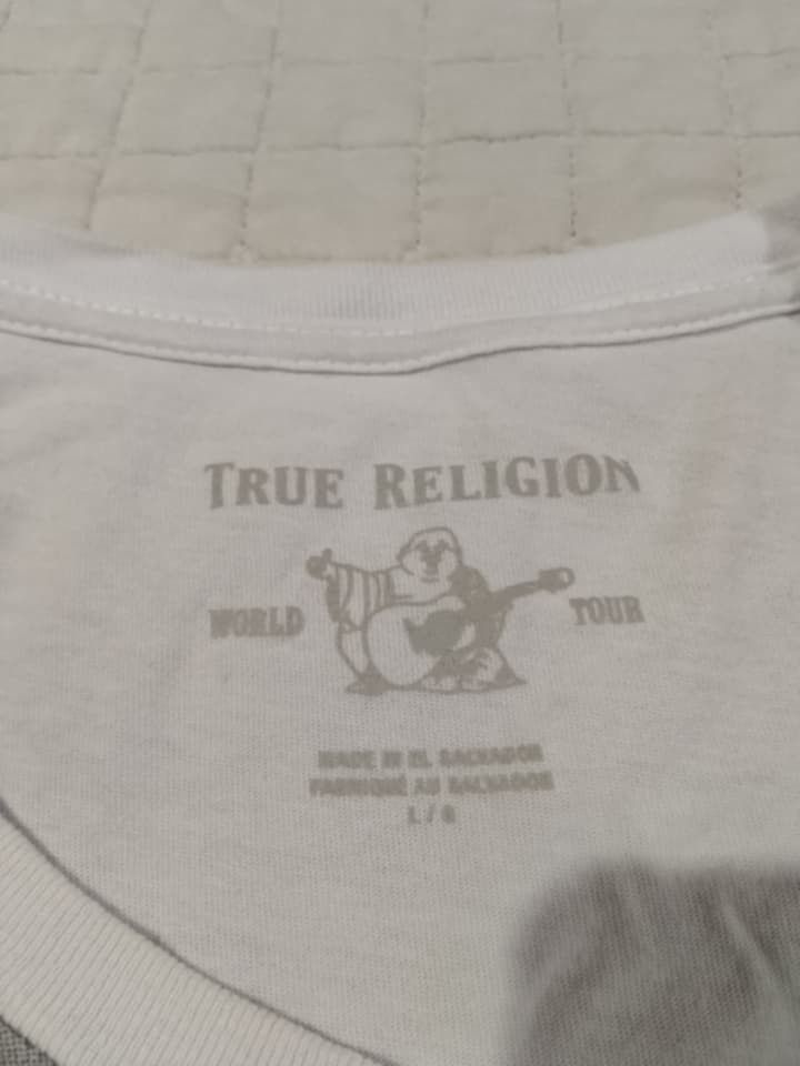 True Religion Men's Graphic T-Shirt (Category: Tshirts & Polo Shirts ) located in Danao, Cebu. Submitted by thriftssfunds (Listing ID 1442634391, Image 3). Description: - White True Religion T-shirt - Size: Large (L) - Features a cool geometric and diagonal graphic print - 'True Religion' logo printed across the chest - Material: 100% Cotton - Made in El Salvador -20.5 W x 29 L -Issue Super Small pinhole sa sleeve not visible.
