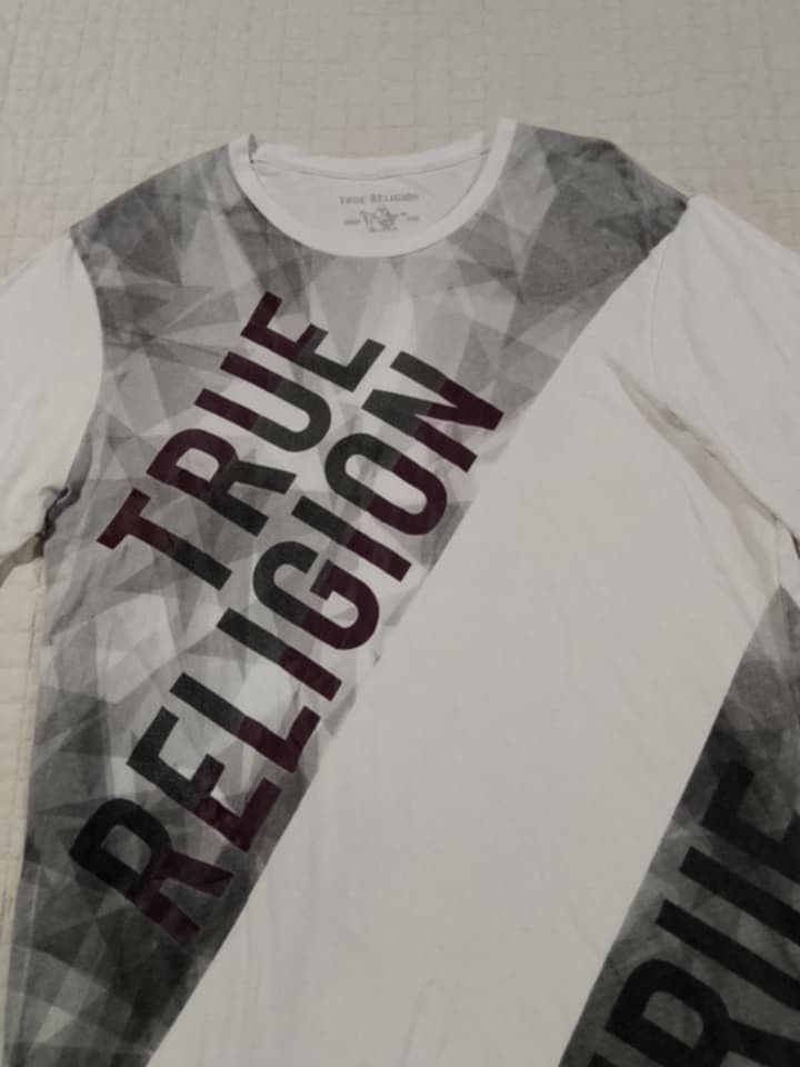True Religion Men's Graphic T-Shirt (Category: Tshirts & Polo Shirts ) located in Danao, Cebu. Submitted by thriftssfunds (Listing ID 1442634391, Image 2). Description: - White True Religion T-shirt - Size: Large (L) - Features a cool geometric and diagonal graphic print - 'True Religion' logo printed across the chest - Material: 100% Cotton - Made in El Salvador -20.5 W x 29 L -Issue Super Small pinhole sa sleeve not visible.