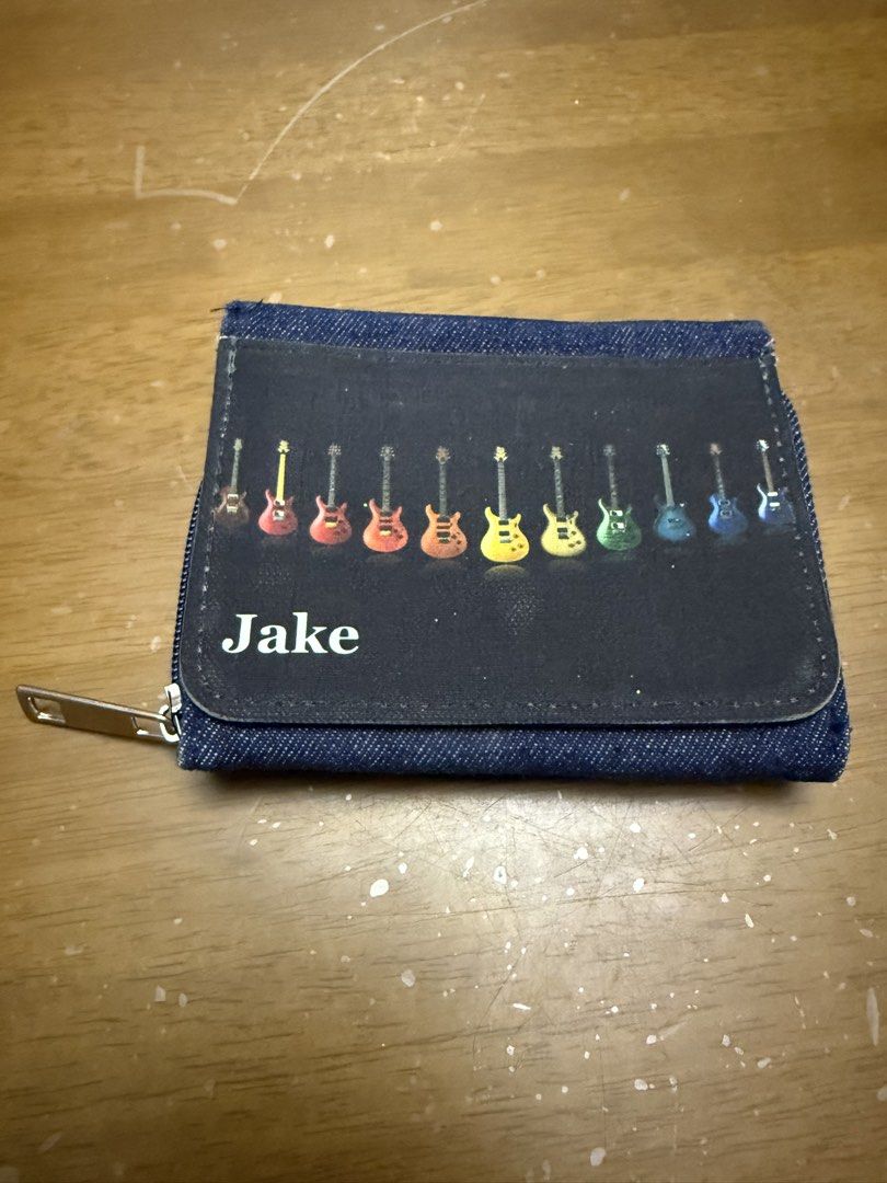 Denim Tri-Fold Wallet with Guitar Design (Category: Wallets & Card holders) located in Pilar. Submitted by faveanyshop (Listing ID 1442763262, Image 1). Description: - Adorable denim wallet - Features a row of colorful guitars on the front - Zippered coin pocket on the side - Includes a clear ID window and card slots - Plenty of space for your essentials - 'Jake' is printed on the front.