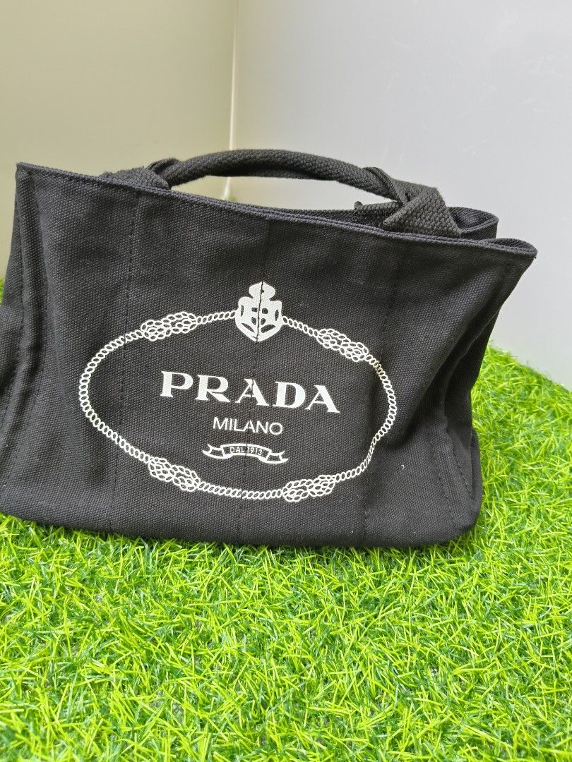 Prada Milano Black Canvas Tote Bag (Category: Luxury Bags & Wallets) located in Manila. Submitted by babylyn85 (Listing ID 1442732328, Image 3). Description: - Classic black Prada tote bag - Durable canvas material - Iconic Prada Milano logo on the front - Interior zipped pocket - Two side pockets - Sturdy and comfortable handles - Ideal for everyday use or travel.
