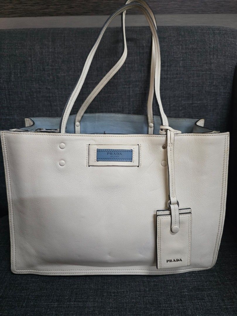 Prada White Leather Tote Bag (Category: Luxury Bags & Wallets) located in General Trias. Submitted by roselle2230 (Listing ID 1442889282, Image 1). Description: - Authentic Prada white leather tote bag - Features iconic Prada logo tag and a smaller luggage tag - Chic light blue interior lining - Secure zipper closure - Ideal size for daily essentials and everyday use.