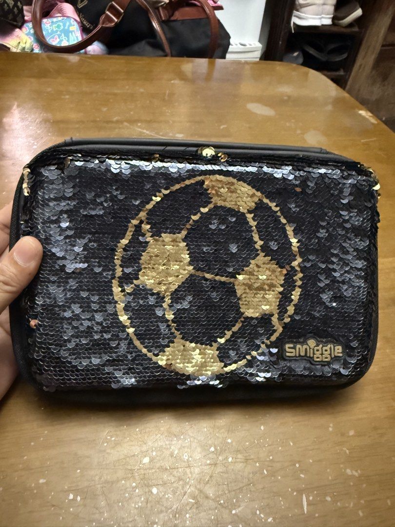 Smiggle Reversible Sequin Pencil Case - Soccer Theme (Category: Babies & Kids Fashion) located in Pilar. Submitted by faveanyshop (Listing ID 1442764359, Image 1). Description: - Smiggle pencil case with fun reversible sequins. - Flip sequins to change design: black with gold soccer ball to gold and black. - Back features a cool soccer print. - Multiple compartments for organizing stationery. - Zippers are in good working condition. - Perfect for