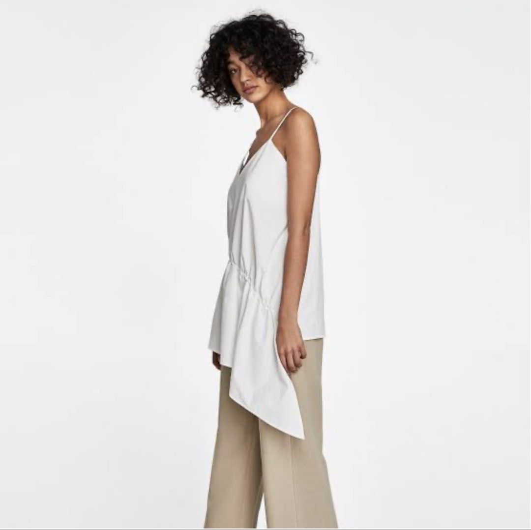 Zara White Asymmetrical Camisole Top (Category: Sleeveless) located in Makati City. Submitted by victoriatrishaa (Listing ID 1442791291, Image 2). Description: White camisole top from Zara. Features a V-neckline and spaghetti straps. W: 26.5” L (short part):27” L (long part):37”.