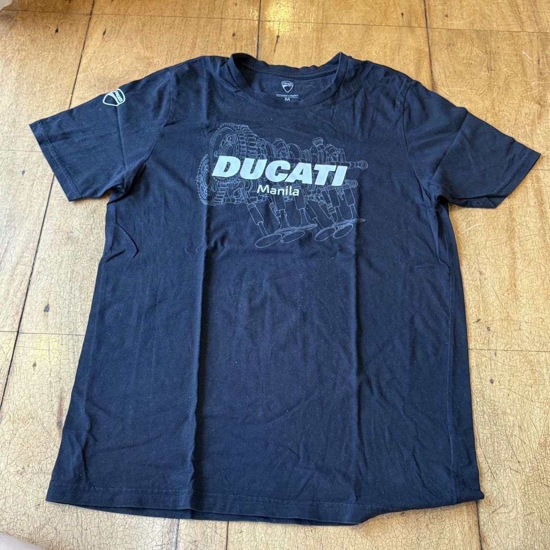 Authentic Ducati Manila Graphic T-Shirt Size M (Category: Tshirts & Polo Shirts ) located in Quezon City. Submitted by brief23 (Listing ID 1447019286, Image 1). Description: - AUTHENTIC Black Ducati T-Shirt (DISCONTINUED DESIGN) - Purchased for ₱2,300 from Ducati Manila - Size: Medium (M) - Features 'DUCATI Manila' text - Graphic print of an engine schematic on the front - Small Ducati logo detail on the left sleeve - Ideal for any Ducati fan or 