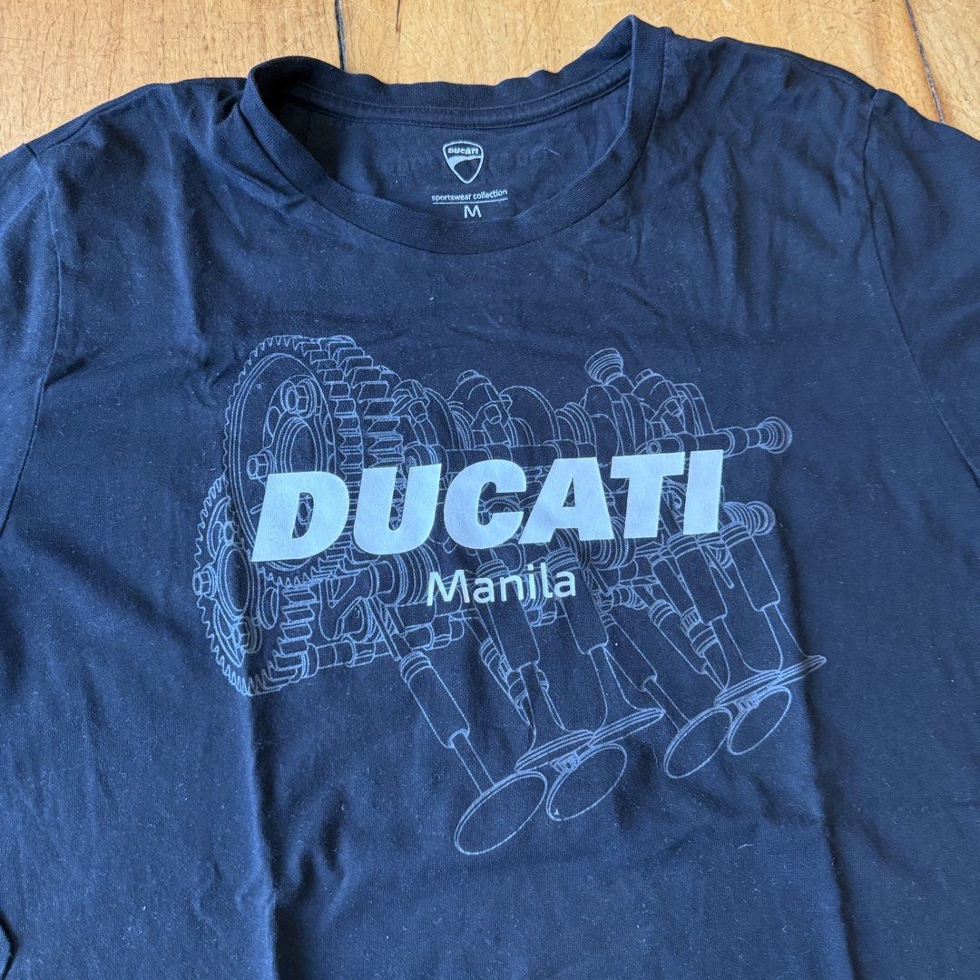 Authentic Ducati Manila Graphic T-Shirt Size M (Category: Tshirts & Polo Shirts ) located in Quezon City. Submitted by brief23 (Listing ID 1447019286, Image 2). Description: - AUTHENTIC Black Ducati T-Shirt (DISCONTINUED DESIGN) - Purchased for ₱2,300 from Ducati Manila - Size: Medium (M) - Features 'DUCATI Manila' text - Graphic print of an engine schematic on the front - Small Ducati logo detail on the left sleeve - Ideal for any Ducati fan or 