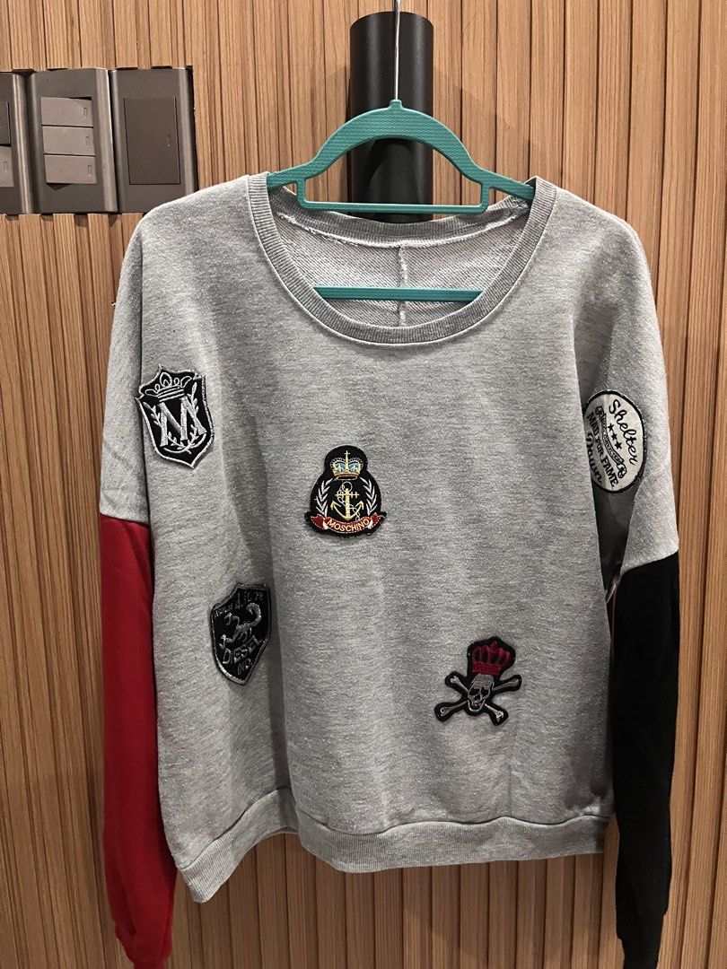 Grey Moschino Patch Sweatshirt with Red & Black Sleeves (Category: Longsleeves) located in Manila. Submitted by lucaaaa_ (Listing ID 1447035332, Image 1). Description: Cool grey sweatshirt with unique patches (Moschino, skull & crossbones, crests). Red/black sleeves. Crew neck. medium to large frame .