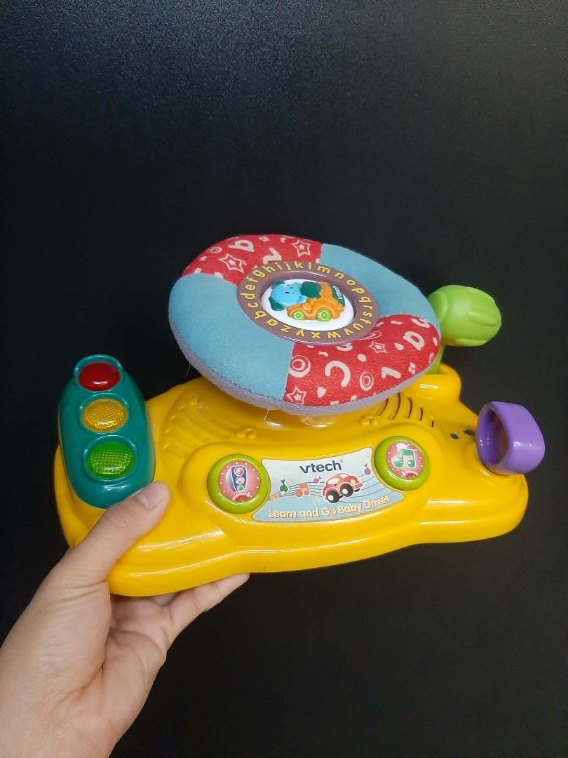 Vtech baby steering wheel with alphabet (Category: Other Babies Going Out Needs) located in Manila. Submitted by sulitfinds_17 (Listing ID 1446955508, Image 1). Description: ✨️This is a VTech Around Town Baby Driver toy featuring a blue fabric steering wheel with alphabet letters. Condition: Working Battery operated The toy includes interactive elements like traffic lights with functioning lights and a horn button. It is designed to help develop 