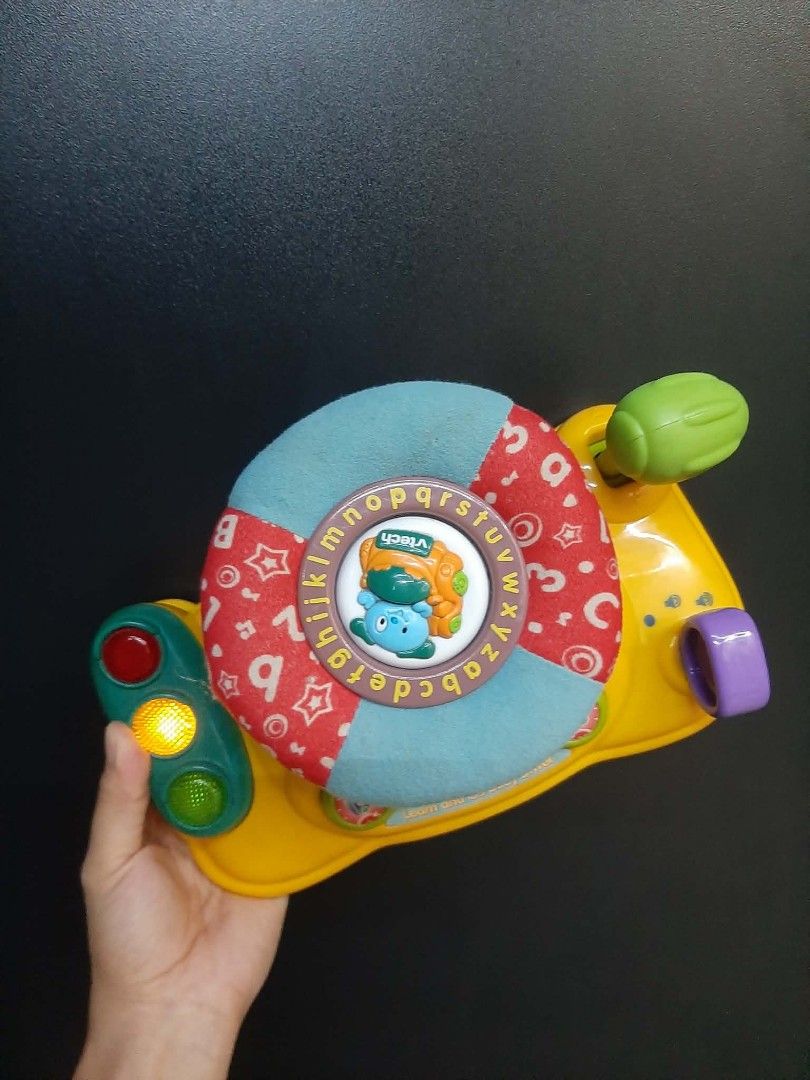 Vtech baby steering wheel with alphabet (Category: Other Babies Going Out Needs) located in Manila. Submitted by sulitfinds_17 (Listing ID 1446955508, Image 2). Description: ✨️This is a VTech Around Town Baby Driver toy featuring a blue fabric steering wheel with alphabet letters. Condition: Working Battery operated The toy includes interactive elements like traffic lights with functioning lights and a horn button. It is designed to help develop 