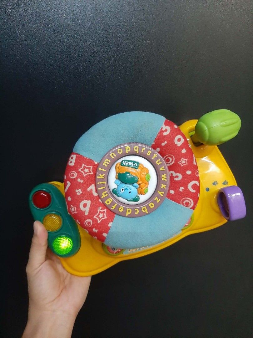 Vtech baby steering wheel with alphabet (Category: Other Babies Going Out Needs) located in Manila. Submitted by sulitfinds_17 (Listing ID 1446955508, Image 3). Description: ✨️This is a VTech Around Town Baby Driver toy featuring a blue fabric steering wheel with alphabet letters. Condition: Working Battery operated The toy includes interactive elements like traffic lights with functioning lights and a horn button. It is designed to help develop 