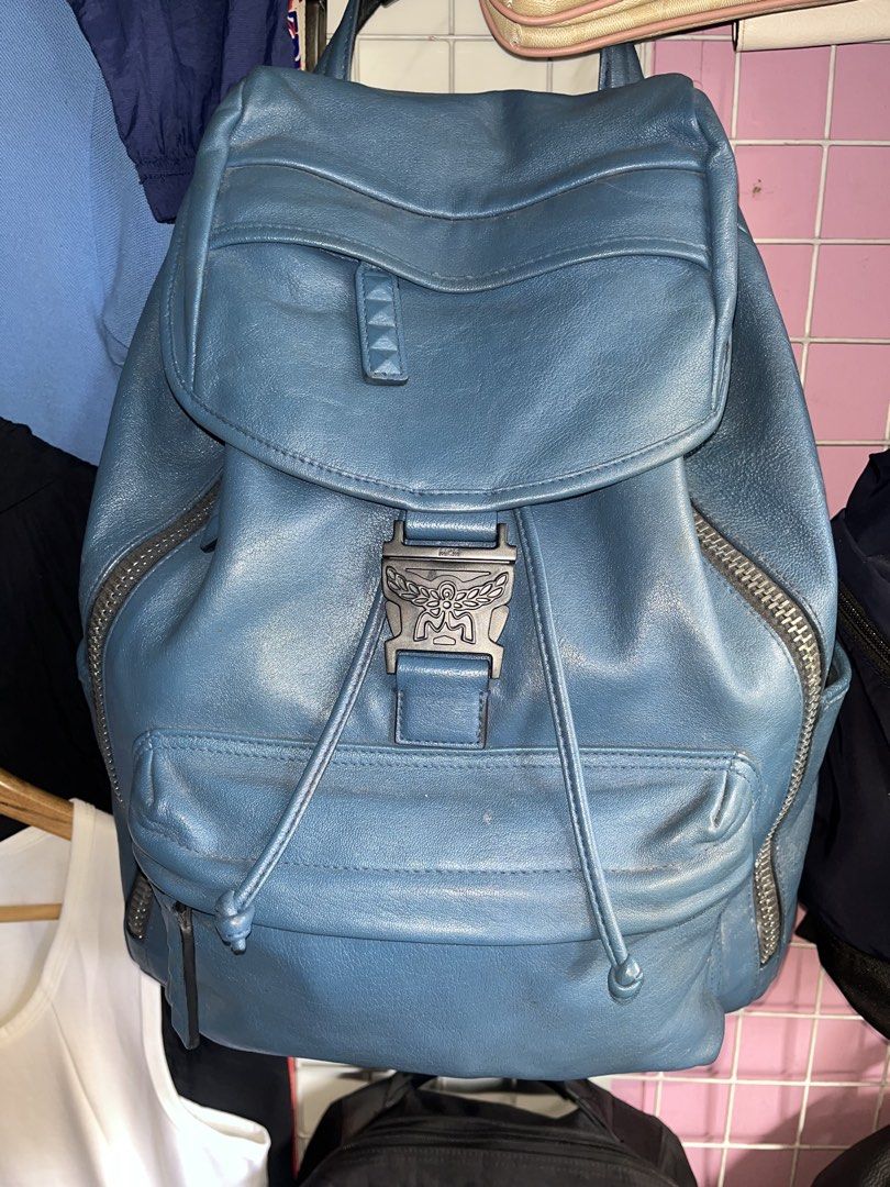 Blue Leather MCM Backpack with Buckle Detail (Category: Luxury Bags & Wallets) located in Carmen. Submitted by by_your_stuff (Listing ID 1448727903, Image 1). Description: - Genuine blue leather MCM backpack - Secure silver buckle closure with MCM logo - Internal drawstring closure for added security - Convenient zipped side pockets - Stylish stud detail on the front flap strap - Minor scuffs on leather, consistent with normal use - Perfect for e