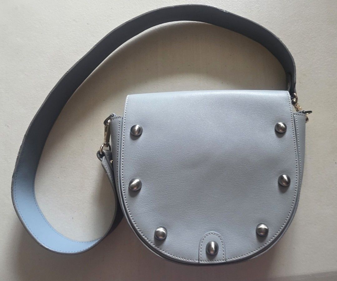 CARLYN Light Blue Leather Saddle Bag with Studs (Category: Cross-body Bags) located in Manila. Submitted by oliviajanuari (Listing ID 1448700464, Image 1). Description: CARLYN Light Blue Leather Saddle Bag with Studs - Color: Light Blue - Style: Saddle Bag - Details: Silver stud embellishments on front flap - Strap: Grey with light blue underside - Closure: Magnetic - Interior: 1 zipped pocket, 1 slip pocket - Perfect for: Everyday use Location: 