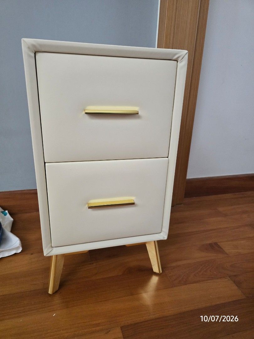 Bedside Table (Category: Tables & Sets) located in Singapore. Submitted by garden.bee (Listing ID 1448706800, Image 2). Description: - Classy bedside table, new! - Cream leather feel - Two drawers with gold handles and gold legs (new and shinny) - Adds a nice touch to any room Brand new, kept in plastic bag..