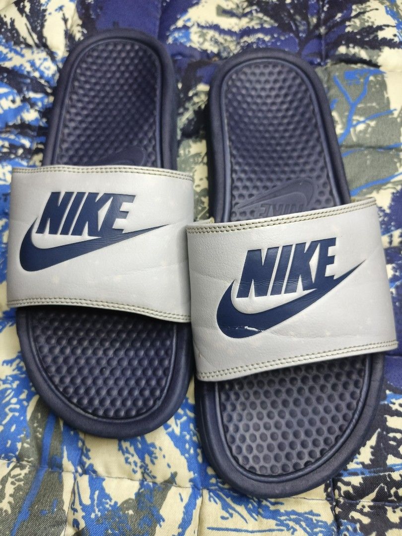 Nike Benassi JDI Slides Navy Blue White (Category: Slippers & Slides) located in Aloran. Submitted by ryban91 (Listing ID 1448889737, Image 1). Description: - Classic Nike slides - Navy blue base with white strap - Iconic Nike swoosh logo - Comfortable for everyday wear or post-sports - Easy slip-on design - Ideal for gym or casual outings.