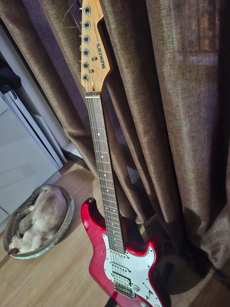 Red Busker's Electric Guitar (Category: Musical Instruments) located in Paranaque City. Submitted by ghanreagan15.1 (Listing ID 1448806273, Image 2). Description: - Red electric guitar - Stratocaster style body - White pickguard - Silver hardware note: slightly rust hardware wilkinson humbucker pickups comes with padded gig bag worth 1.5k guitar stand guitar strap tremolo - 'Busker's' brand on headstock - Ready for a new owner.