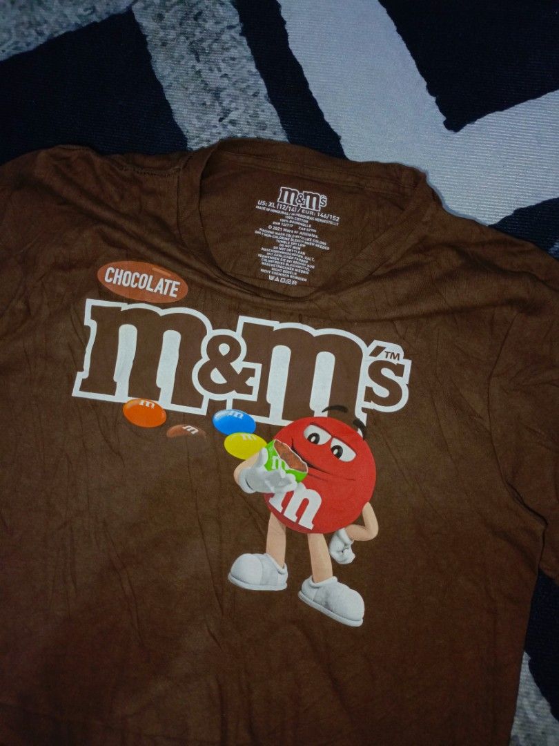 Brown M&M's Graphic T-Shirt (Category: Tshirts & Polo Shirts ) located in Andop. Submitted by kyutoryuu (Listing ID 1449076189, Image 2). Description: M&M's Tee •Dimes: 17.5x24 •Condition: As New •CR: 9.8/10 •Choco Brown •Issue: need wash.