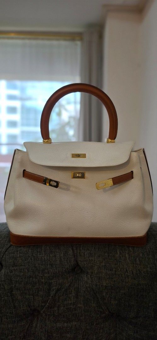 Italian Genuine Leather White Handbag (Category: Luxury Bags & Wallets) located in Manila. Submitted by amc88 (Listing ID 1448946298, Image 2). Description: Made in Italy, this SanCarlo Milano top handle bag features a structured silhouette heavily inspired by the timeless Kelly design. ​Crafted in Italy with a beautiful contrast of crisp cream pebbled leather and rich tan smooth leather trim, this bag elevates any outfit instantly. Material: Pre