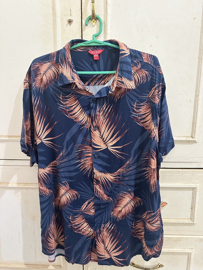 Guess Men's Short Sleeve Button Up Shirt Size L (Category: Tshirts & Polo Shirts ) located in Bugallon. Submitted by lavenderlane (Listing ID 1449144792, Image 1). Description: - Short sleeve button-up shirt - Dark blue base with tropical leaf print - Print colors: Rust and Tan - Button front closure - Size: L - Ideal for casual wear or vacation.