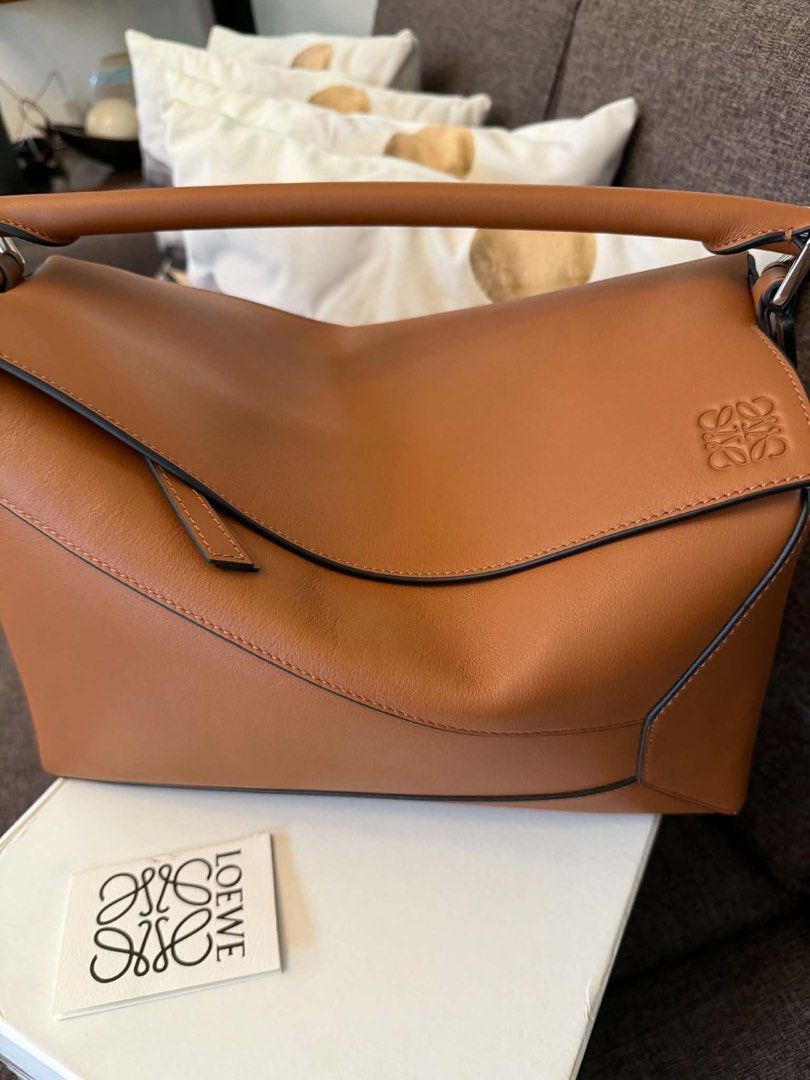 Loewe Puzzle Hobo Bag Tan Leather (Medium Size) (Category: Luxury Bags & Wallets) located in Hermosa. Submitted by bookwormhermosa (Listing ID 1449121408, Image 2). Description: - Loewe Puzzle - Color: Tan leather - Includes original box and dust bag - Detachable shoulder strap included - Features the iconic Loewe Anagram logo - Ideal for everyday use - Spacious interior.