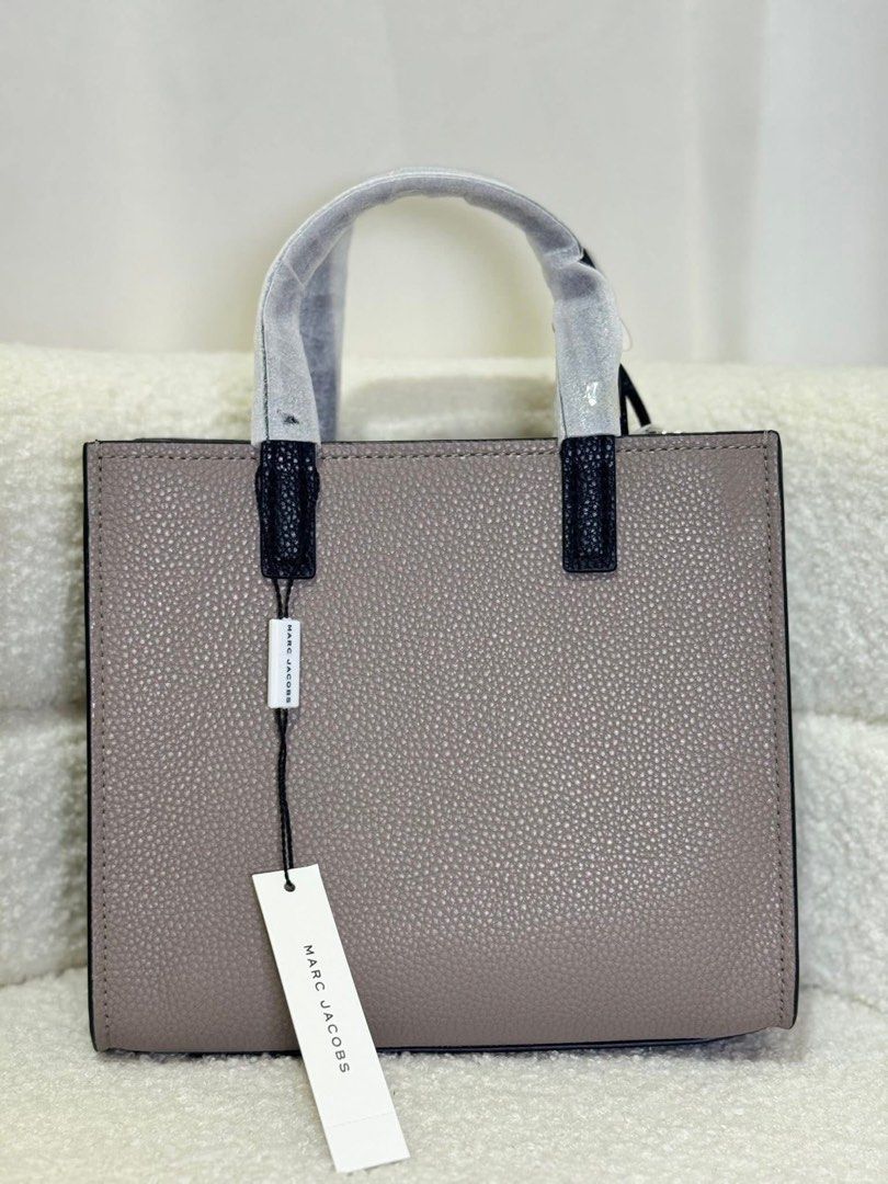 Marc Jacobs The Tote Bag Mini Grind (Category: Luxury Bags & Wallets) located in Batangas. Submitted by theprelovedfinds (Listing ID 1449322572, Image 3). Description: - Authentic Marc Jacobs Mini Tote Bag - Color: Taupe pebbled leather - Cream front pocket with black "MARC JACOBS" logo - Black top handles and trim - Detachable shoulder strap included - Interior zip pocket - Comes with original dust bag and tags.
