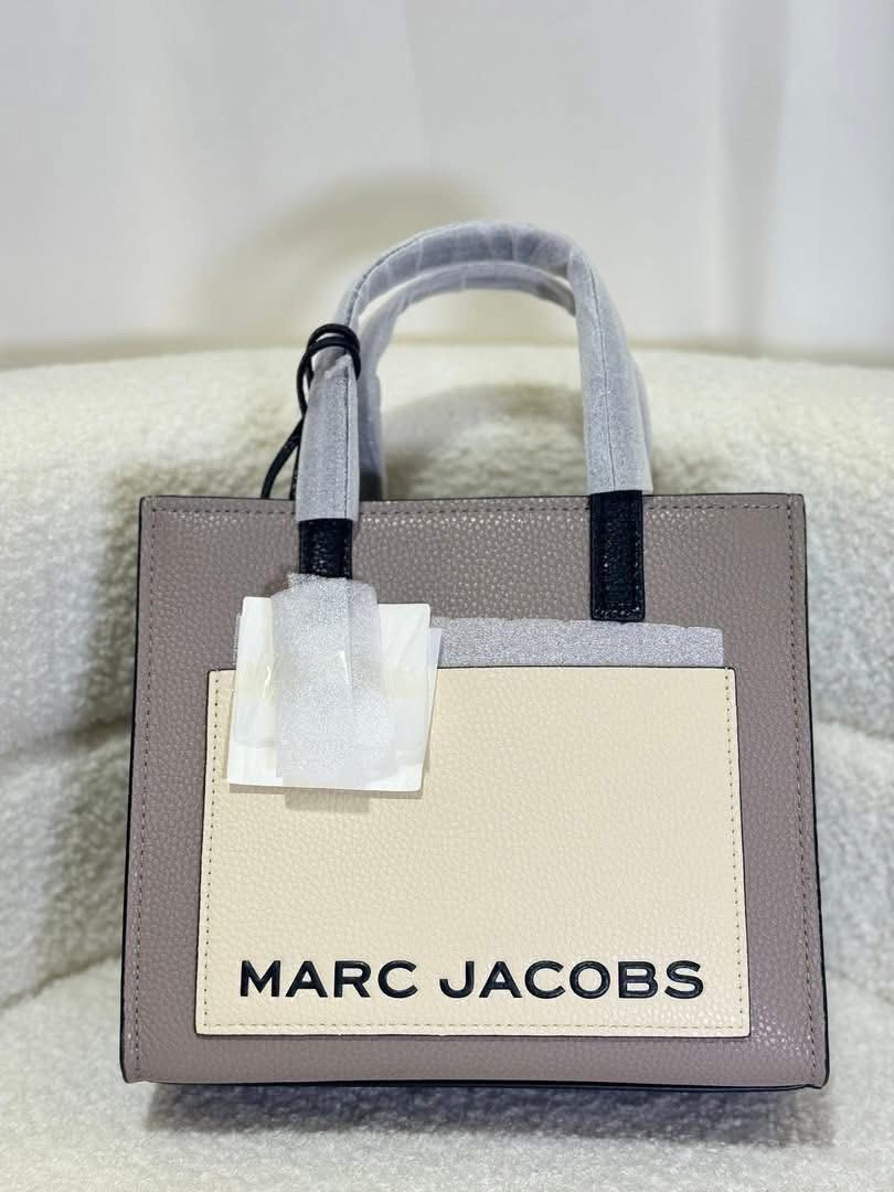 Marc Jacobs The Tote Bag Mini Grind (Category: Luxury Bags & Wallets) located in Batangas. Submitted by theprelovedfinds (Listing ID 1449322572, Image 1). Description: - Authentic Marc Jacobs Mini Tote Bag - Color: Taupe pebbled leather - Cream front pocket with black "MARC JACOBS" logo - Black top handles and trim - Detachable shoulder strap included - Interior zip pocket - Comes with original dust bag and tags.