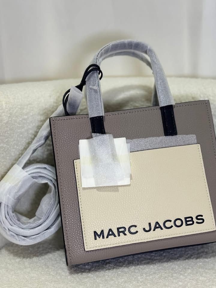 Marc Jacobs The Tote Bag Mini Grind (Category: Luxury Bags & Wallets) located in Batangas. Submitted by theprelovedfinds (Listing ID 1449322572, Image 2). Description: - Authentic Marc Jacobs Mini Tote Bag - Color: Taupe pebbled leather - Cream front pocket with black "MARC JACOBS" logo - Black top handles and trim - Detachable shoulder strap included - Interior zip pocket - Comes with original dust bag and tags.