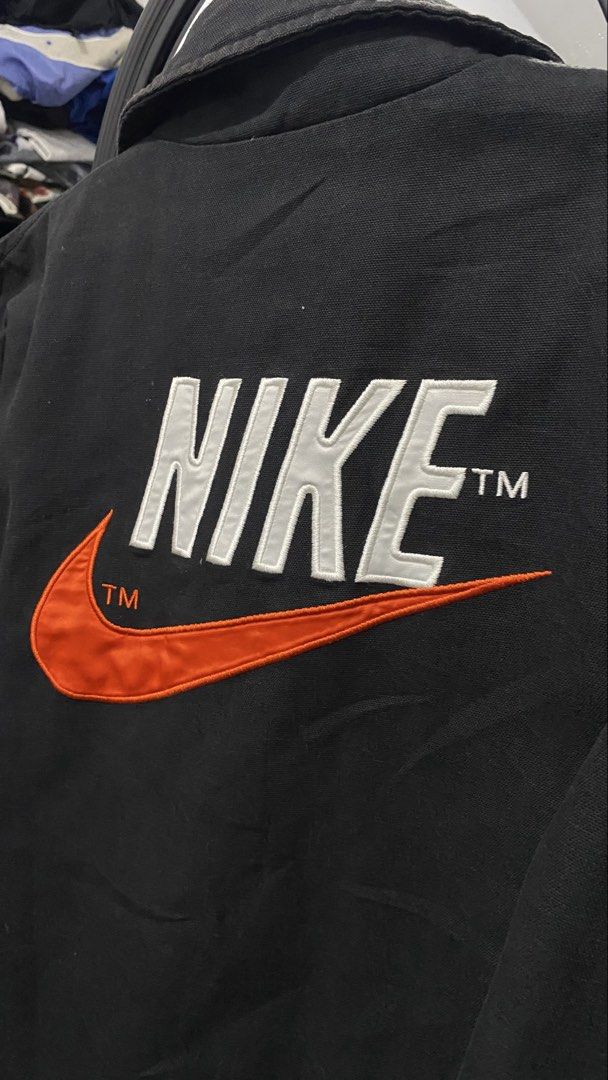 Nike Black Coach Jacket with Swoosh Logo (Category: Coats, Jackets and Outerwear) located in Porac. Submitted by moethrifter (Listing ID 1449167059, Image 2). Description: - Classic black Nike coach jacket - Iconic orange swoosh and Nike logo embroidered on back - Quilted lining for added warmth - Snap button closure - Two side pockets - Ideal for everyday wear.