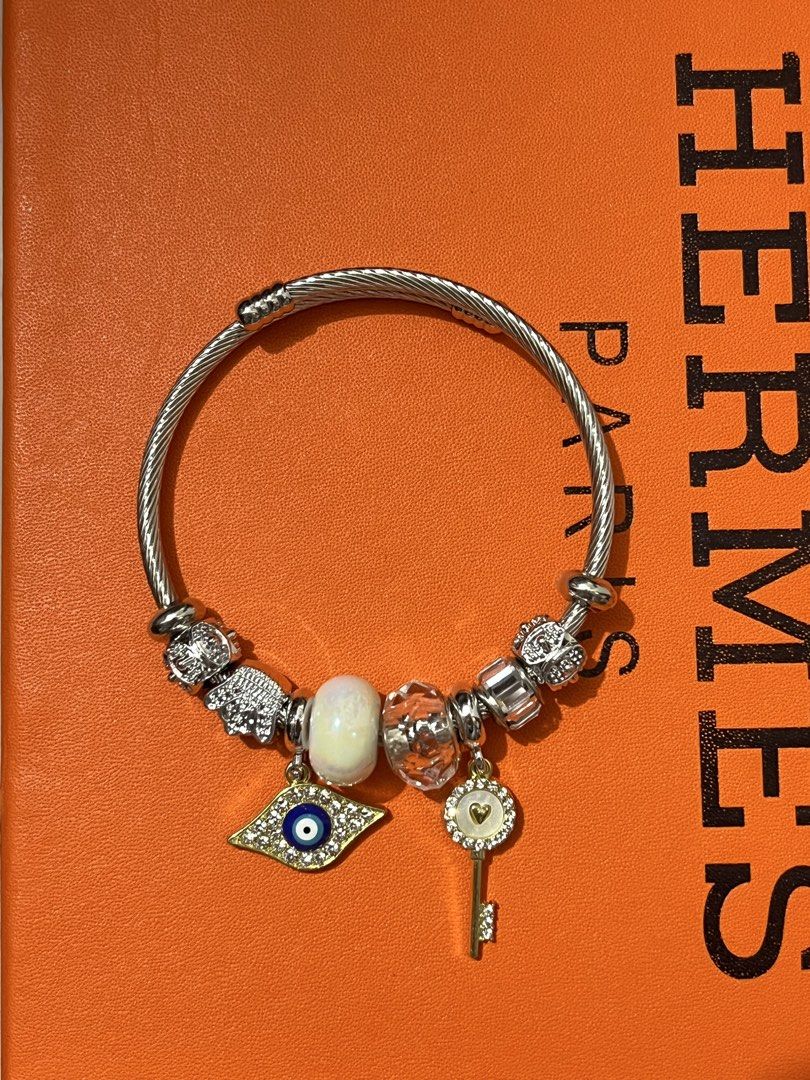 Silver Bangle Bracelet with Evil Eye and Key Charm (Category: Bracelets) located in Paranaque City. Submitted by kyriaki_thrift_shop (Listing ID 1449221735, Image 2). Description: - Silver cable chain bracelet - Features an evil eye charm with blue and gold details - Includes a gold key charm with a heart - Adorned with clear and iridescent beads - Clasp closure - Pandora style design.