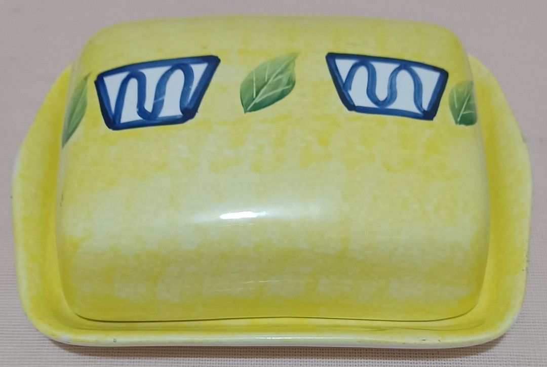 🧈 Hand-Painted Ceramic Butter Dish (Category: Other Kitchenware & Tableware) located in Quezon City. Submitted by wjmae (Listing ID 1449429551, Image 1). Description: Item Details: - Design: Bright yellow marbled finish with hand-painted blue geometric accents + green leaf details; classic country/kitchen style ​ - Size: Approx 6.75 in × 5.25 in base, fits standard 250g/1lb butter blocks perfectly ​ - Material: Glossy glazed ceramic, easy to cle