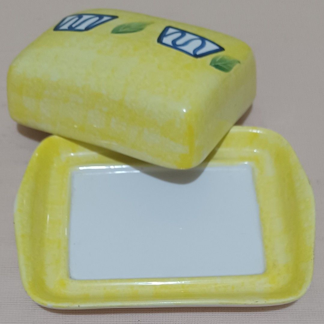 🧈 Hand-Painted Ceramic Butter Dish (Category: Other Kitchenware & Tableware) located in Quezon City. Submitted by wjmae (Listing ID 1449429551, Image 2). Description: Item Details: - Design: Bright yellow marbled finish with hand-painted blue geometric accents + green leaf details; classic country/kitchen style ​ - Size: Approx 6.75 in × 5.25 in base, fits standard 250g/1lb butter blocks perfectly ​ - Material: Glossy glazed ceramic, easy to cle