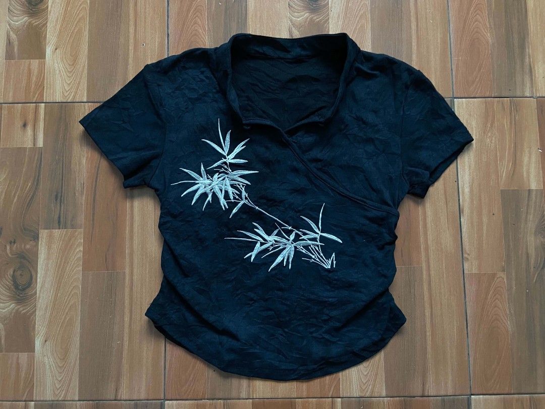 Black Short Sleeve Top with Bamboo Print (Category: Blouses) located in Nabua. Submitted by chic-rack (Listing ID 1449421707, Image 2). Description: - Black short sleeve top - Features a wrap-style front - Mandarin collar - White bamboo leaf print on the front - Textured fabric - Versatile for casual or slightly dressy looks - Subtle ruching details on the sides - Curved hemline - Price+SF.