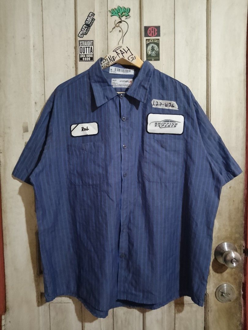 Blue Striped Work Shirt with Patches (Category: Tshirts & Polo Shirts ) located in Naga. Submitted by neppyboy (Listing ID 1449497214, Image 1). Description: - Blue work shirt with vertical pinstripes - Two chest pockets - One pocket patch: 'Rob' - Other pocket patch: 'L27-W26 SHIPPING EXPERTS' with graphic - Button-up front - Short sleeves - Ideal for casual wear or costumes.