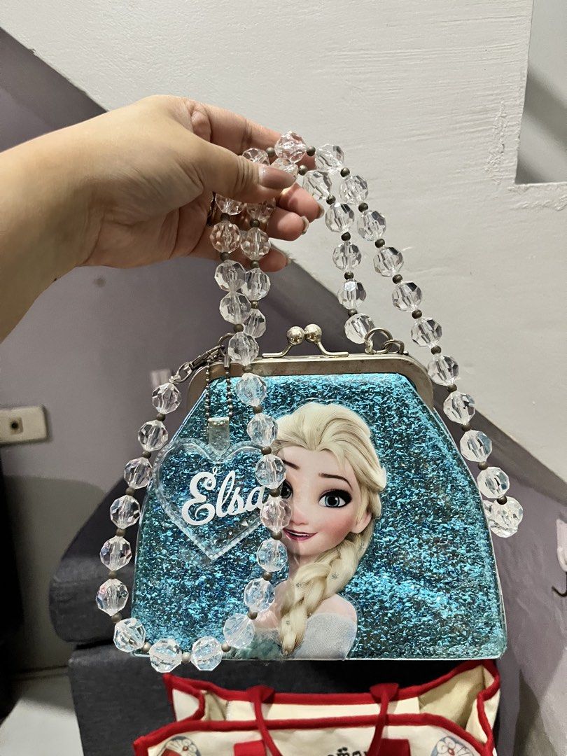 Elsa Frozen Glitter Handbag with Beaded Strap (Category: Purses & Pouches) located in Angono. Submitted by dubibo (Listing ID 1449475284, Image 2). Description: - Cute Elsa handbag with a glittery blue finish. - Features a heart-shaped charm with 'Elsa' on it. - Clear bead strap for a stylish touch. - Blue fabric lining inside. - Ideal gift for any Frozen enthusiast!.