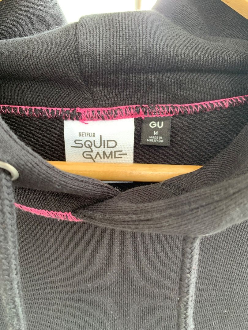 GU Squid Game Black Hoodie Size M (Category: Coats, Jackets and Outerwear) located in Malolos. Submitted by jr0nhele08 (Listing ID 1449370931, Image 3). Description: - Black hoodie with iconic Squid Game logo on front. - Features stylish pink stitching details. - Made from 100% cotton with added spandex for a comfortable stretch. - Ideal for casual wear and showing off your fandom. Dimensions: width 21" length 25".