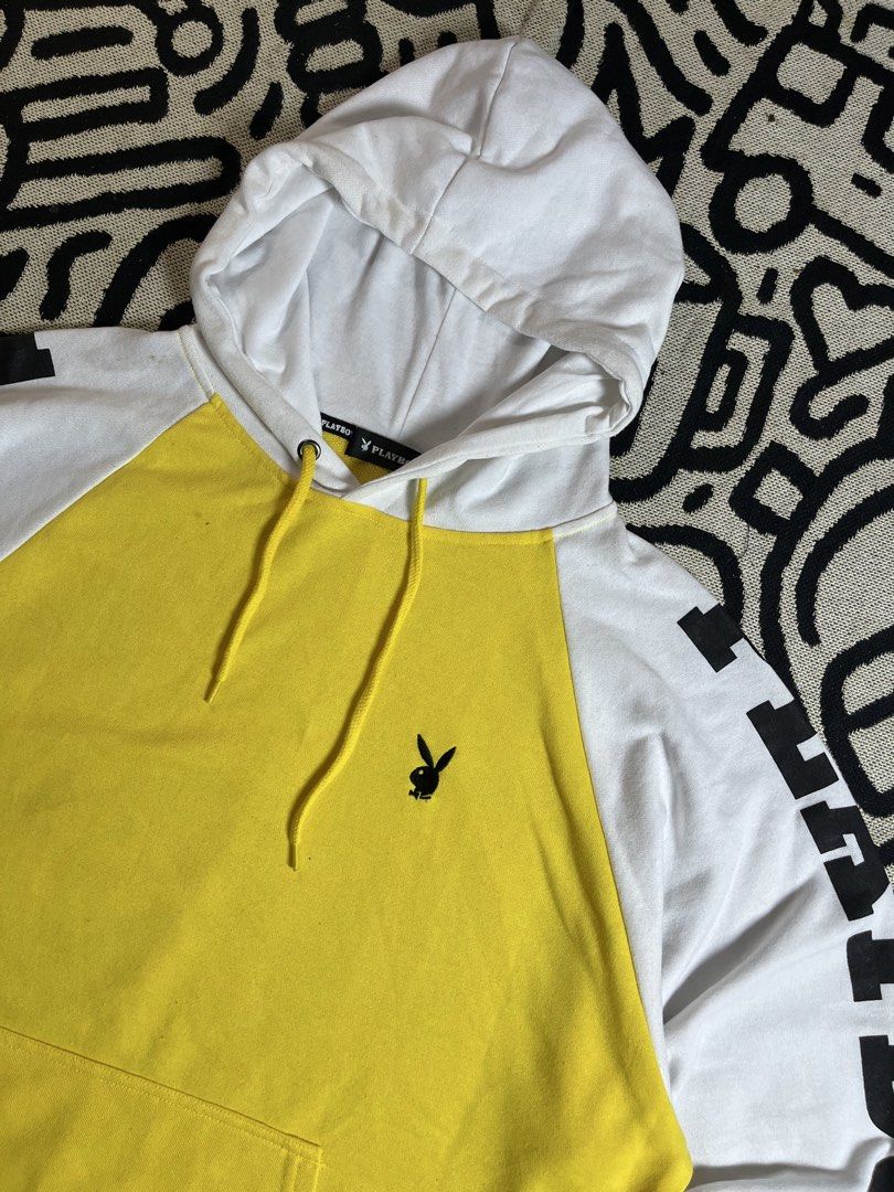 Playboy Yellow & White Raglan Hoodie (Category: Hoodies) located in Silang. Submitted by yusthrift (Listing ID 1449346030, Image 2). Description: - Playboy raglan hoodie in yellow and white. - Features the iconic Playboy bunny logo on the front. - 'PLAYBOY' text graphic printed on the sleeves. - Convenient kangaroo pocket for your essentials. - Adjustable drawstring hood for a comfortable fit. - Ideal for everyday casual wear. Size: L on tag 24.5