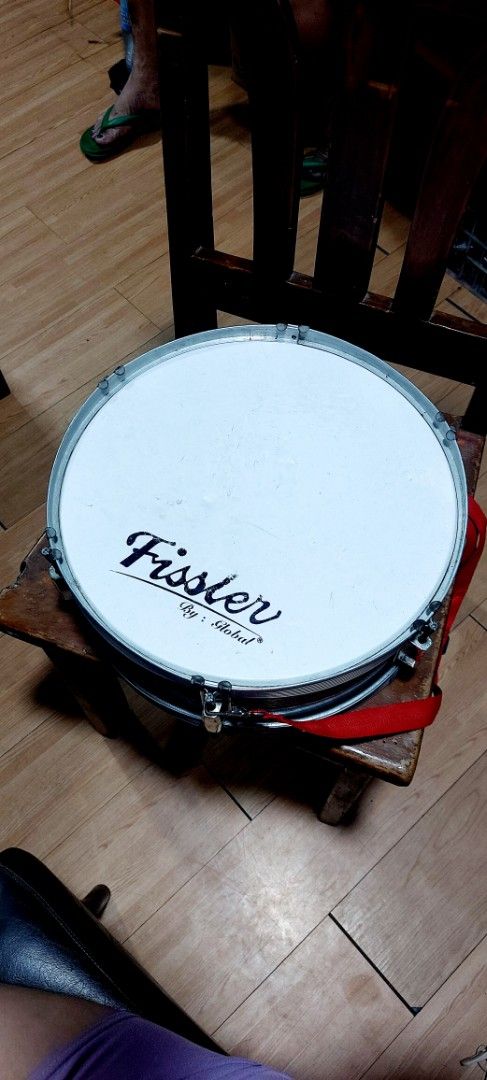 Fissler By Global Snare Drum (Category: Musical Instruments) located in Quezon City. Submitted by tinypeep.ph (Listing ID 1449678786, Image 1). Description: - Fissler snare drum by Global - Features a red strap - Drum head shows some bubbling and wear - Snare wires are attached and functional - Ideal for practice sessions or beginner drummers.